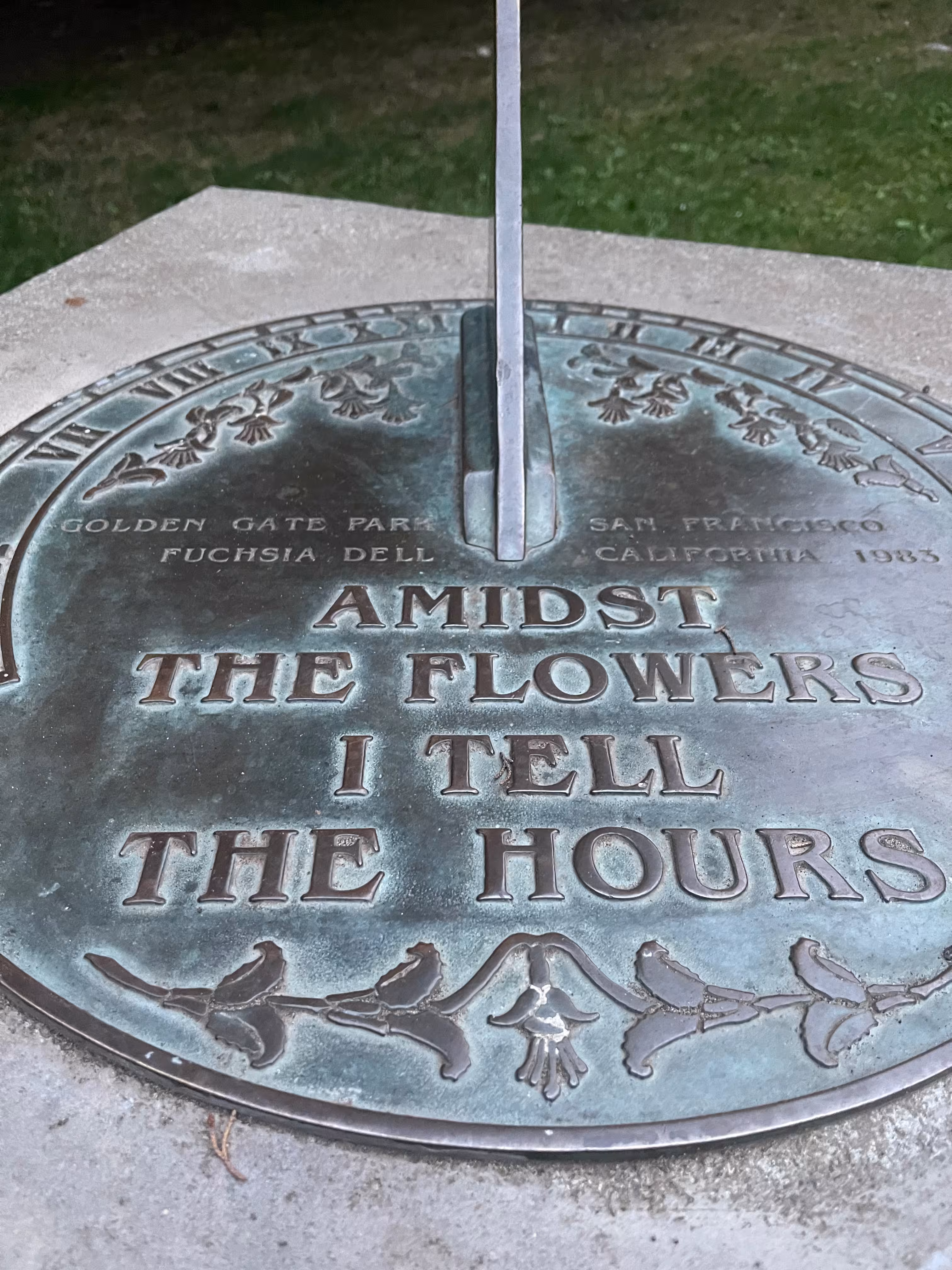 The sundial in the Fuchsia Dell. The inscription reads 'Among the flowers I tell the hours'.